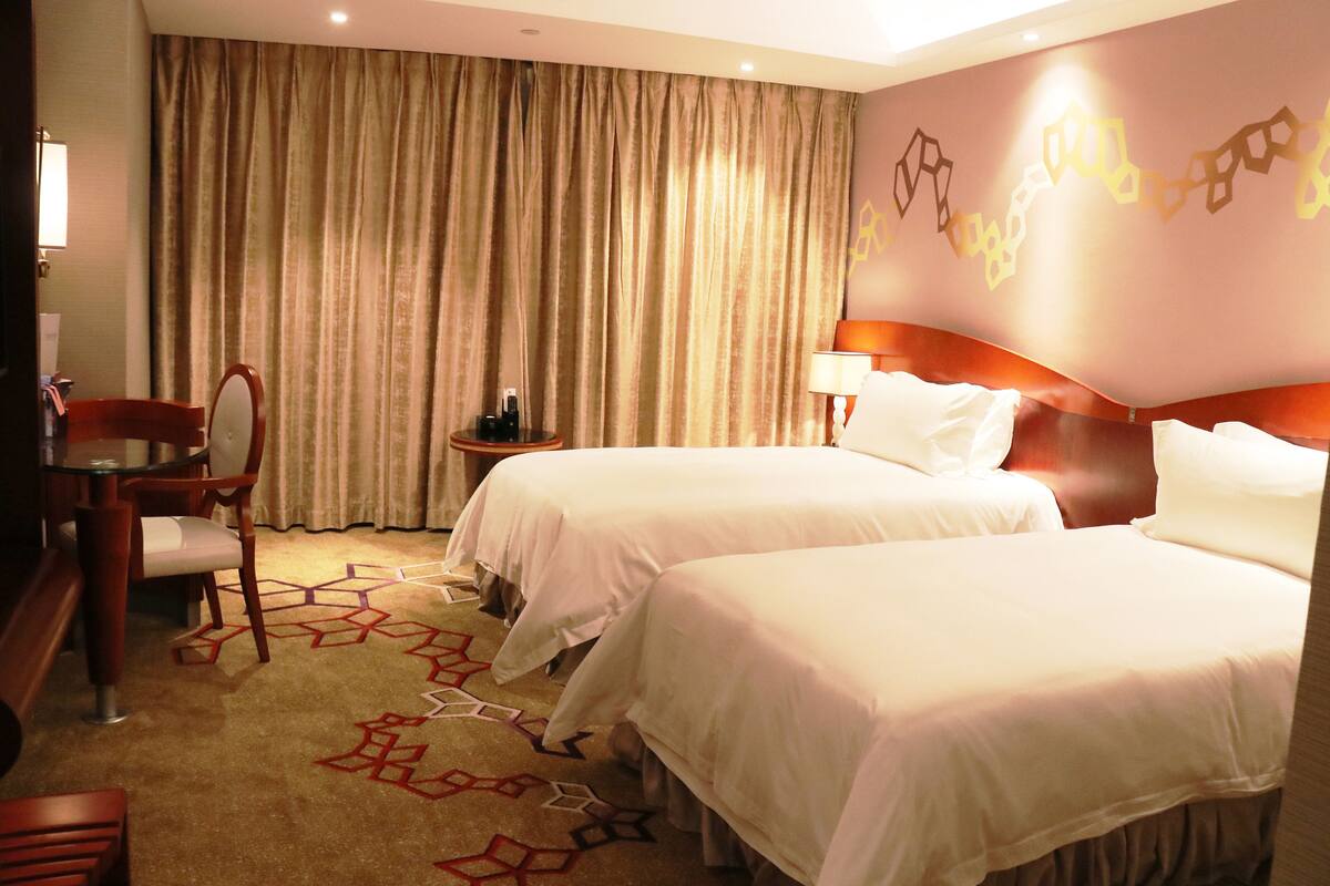 Ein Hotelzimmer mit zwei Betten, einem Schreibtisch mit Stuhl, einer Lampe und einem Vorhang.