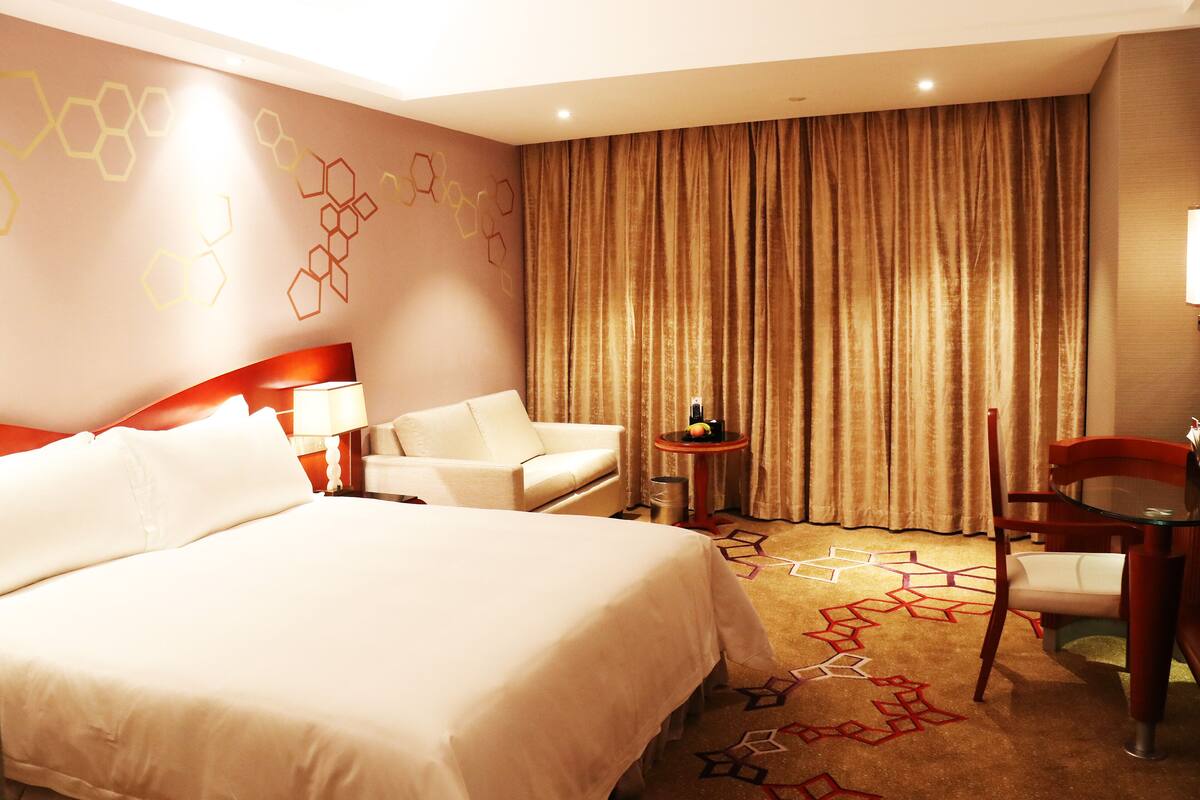 Ein Hotelzimmer mit einem großen Bett, einem Schreibtisch, einem Stuhl und einem kleinen Tisch mit einer Lampe.