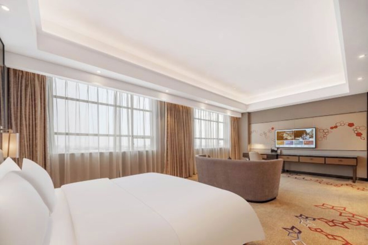 A hotel room with a large bed, a seating area, a flat-screen TV, and a decorative wall.