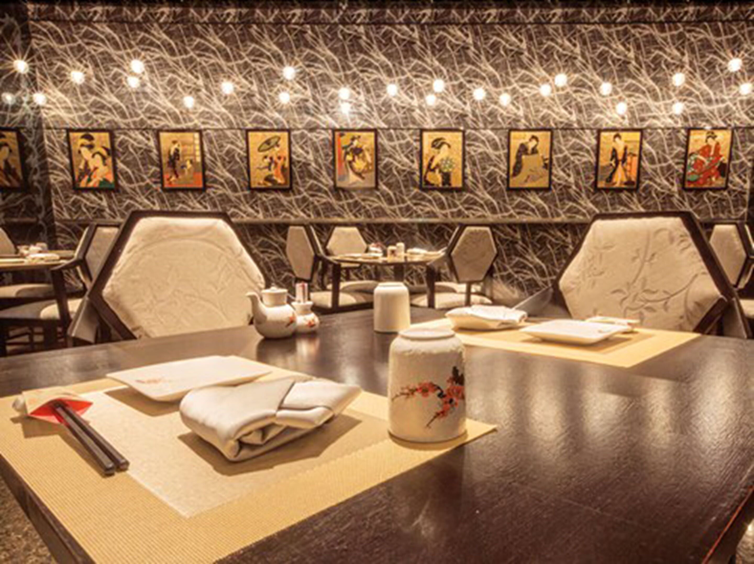 L’intérieur d’un restaurant, avec des tables dressées pour le service, des chaises et un mur décoratif orné d’œuvres d’art encadrées.