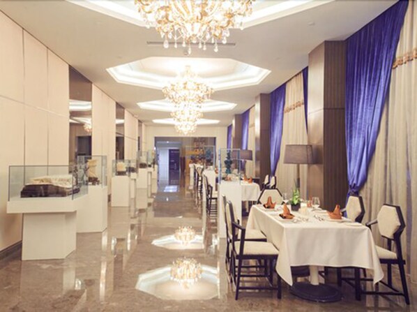 Un amplio vestíbulo de hotel con techo alto, candelabros y un largo pasillo que conduce a un comedor con mesas y sillas.