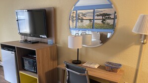 A compact hotel room with a wooden desk, a chair, a television, a microwave, a small trash bin, and a wall-mounted lamp. - Days Inn by Wyndham Fordyce (Fordyce)