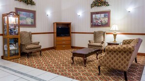 A room with patterned carpet, two armchairs, a wooden coffee table, a television, and a cabinet with framed pictures. - Days Inn by Wyndham Fordyce (Fordyce)