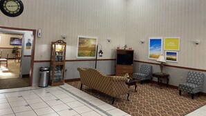 A hotel lobby with a patterned carpet, a sofa, patterned chairs, a television, a clock, and framed pictures on the wall. - Days Inn by Wyndham Fordyce (Fordyce)