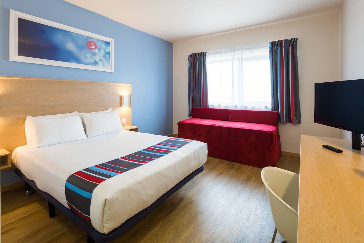 Ein Hotelzimmer mit Bett, Nachttisch, Fernseher und einem Fenster mit Vorhängen.