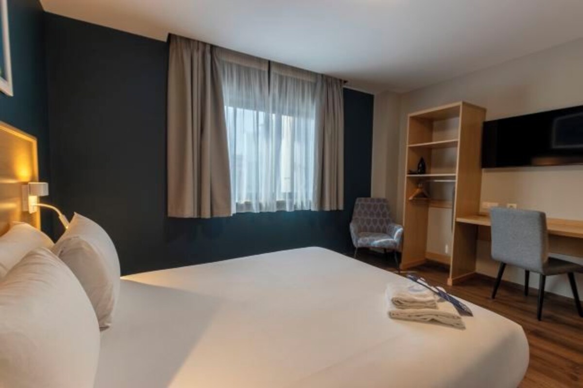 Une chambre d’hôtel avec un grand lit, un bureau, une chaise, une télévision et une armoire.