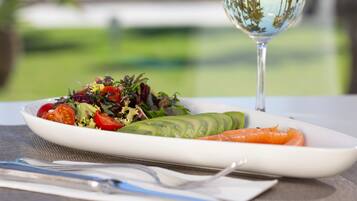 Un plato blanco con ensalada, una rebanada de aguacate y una zanahoria, acompañado de una copa de vino blanco sobre una mesa.