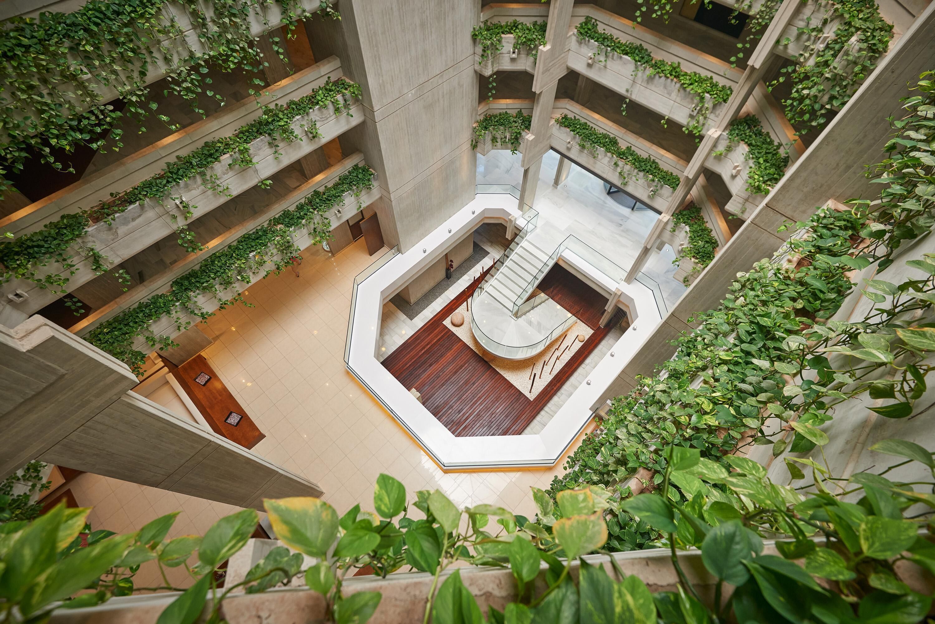 A multi-level atrium with concrete pillars, wooden flooring, and green plants.