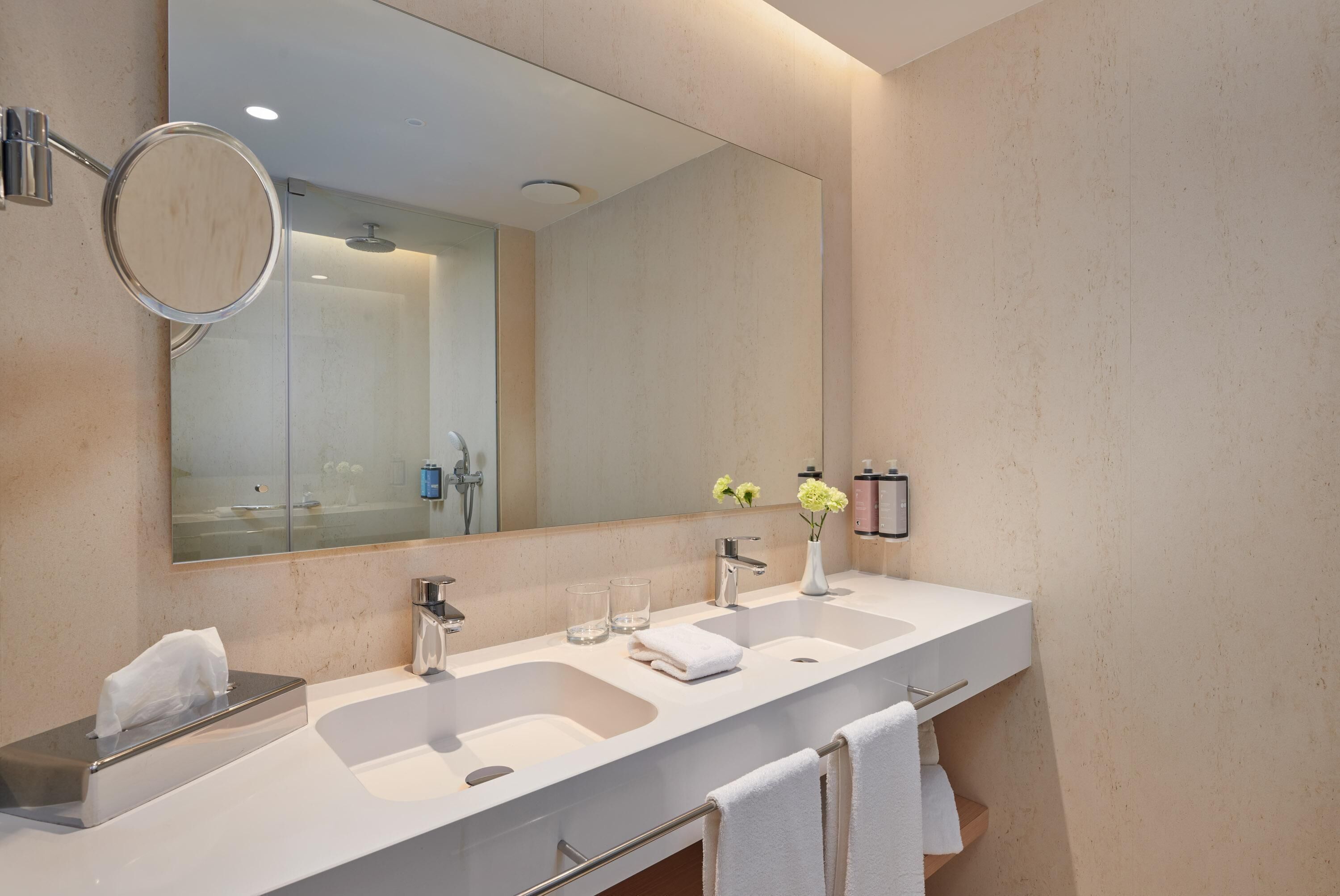 A modern bathroom with two sinks, a large mirror, a towel rack, and a glass shower enclosure.