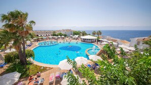 A large outdoor swimming pool with multiple lanes, surrounded by lounge chairs and umbrellas, with a view of the sea in the background. - Blau Punta Reina (Manacor)