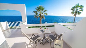 A balcony with a table and chairs, a view of the sea, and palm trees. - Blau Punta Reina (Manacor)
