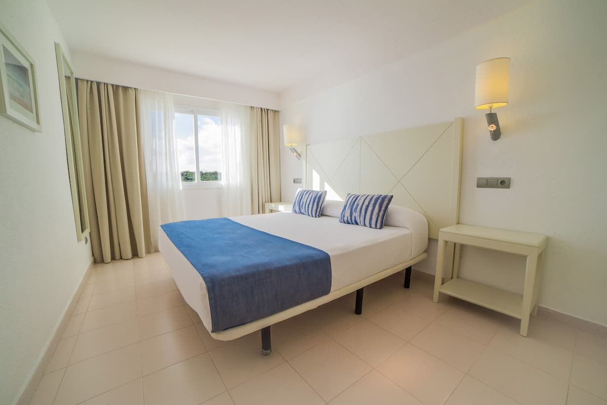 A hotel room with a large bed, a bedside table, a lamp, and a window with curtains.