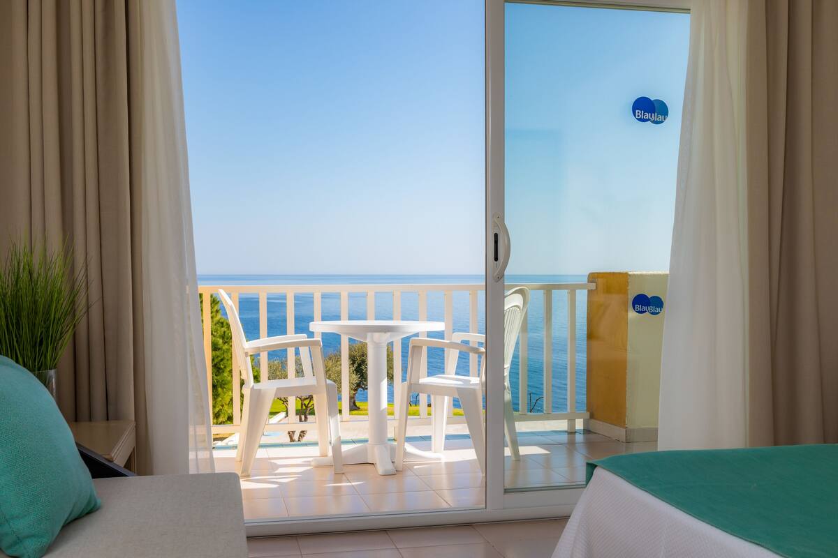 A balcony with a view of the sea, white furniture, and a sign with "Blaulau" on it.