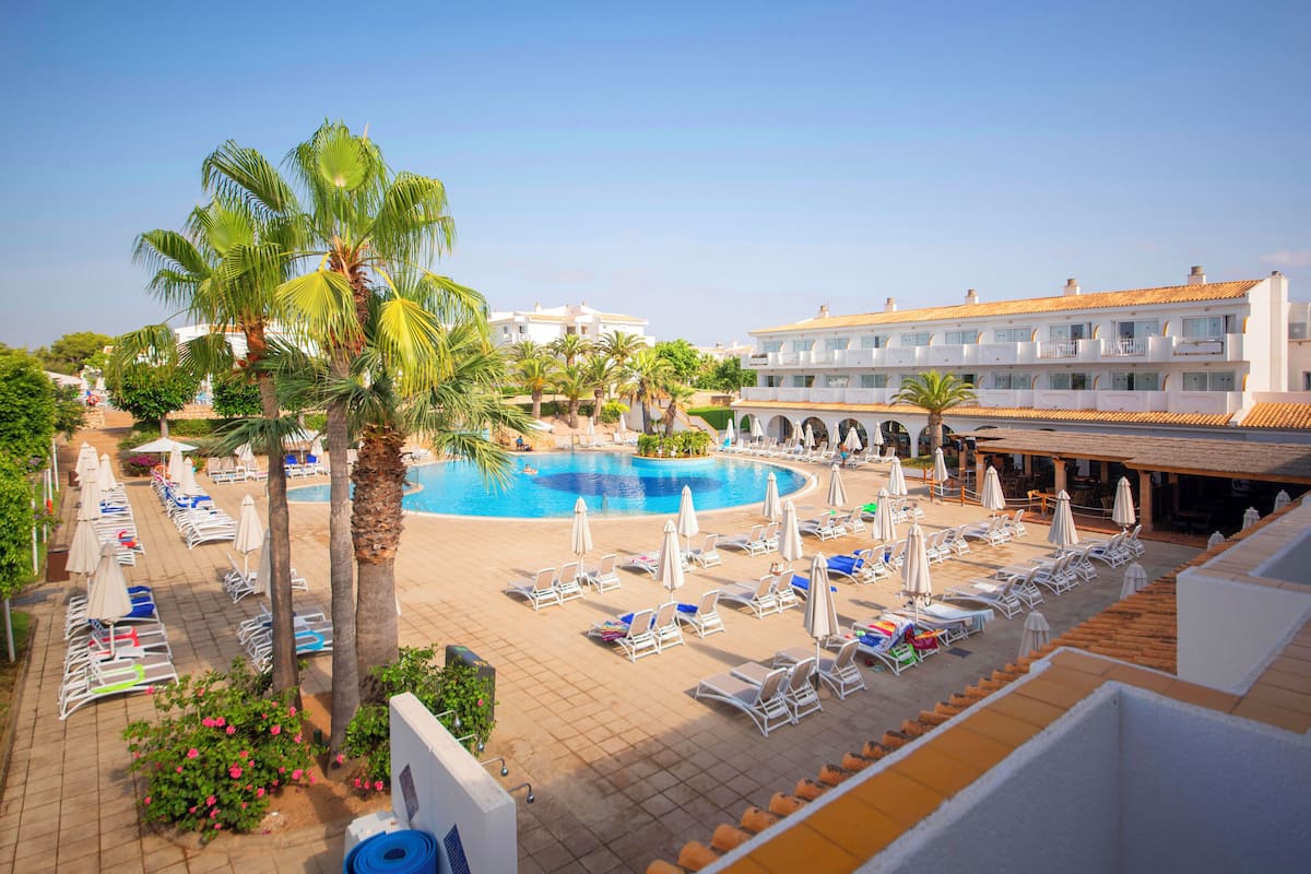 A hotel with a swimming pool, sun loungers, and palm trees.