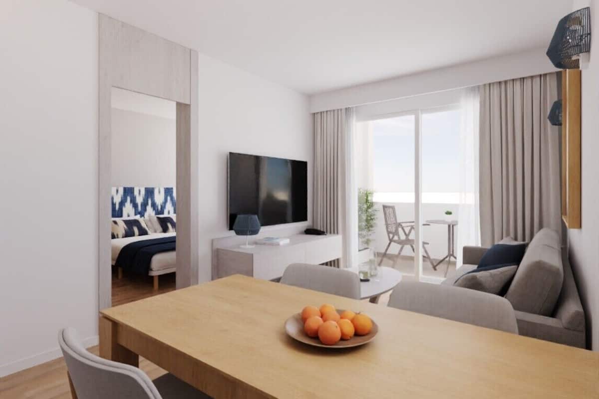 A modern living room with a wooden dining table, a sofa, and a TV mounted on the wall.