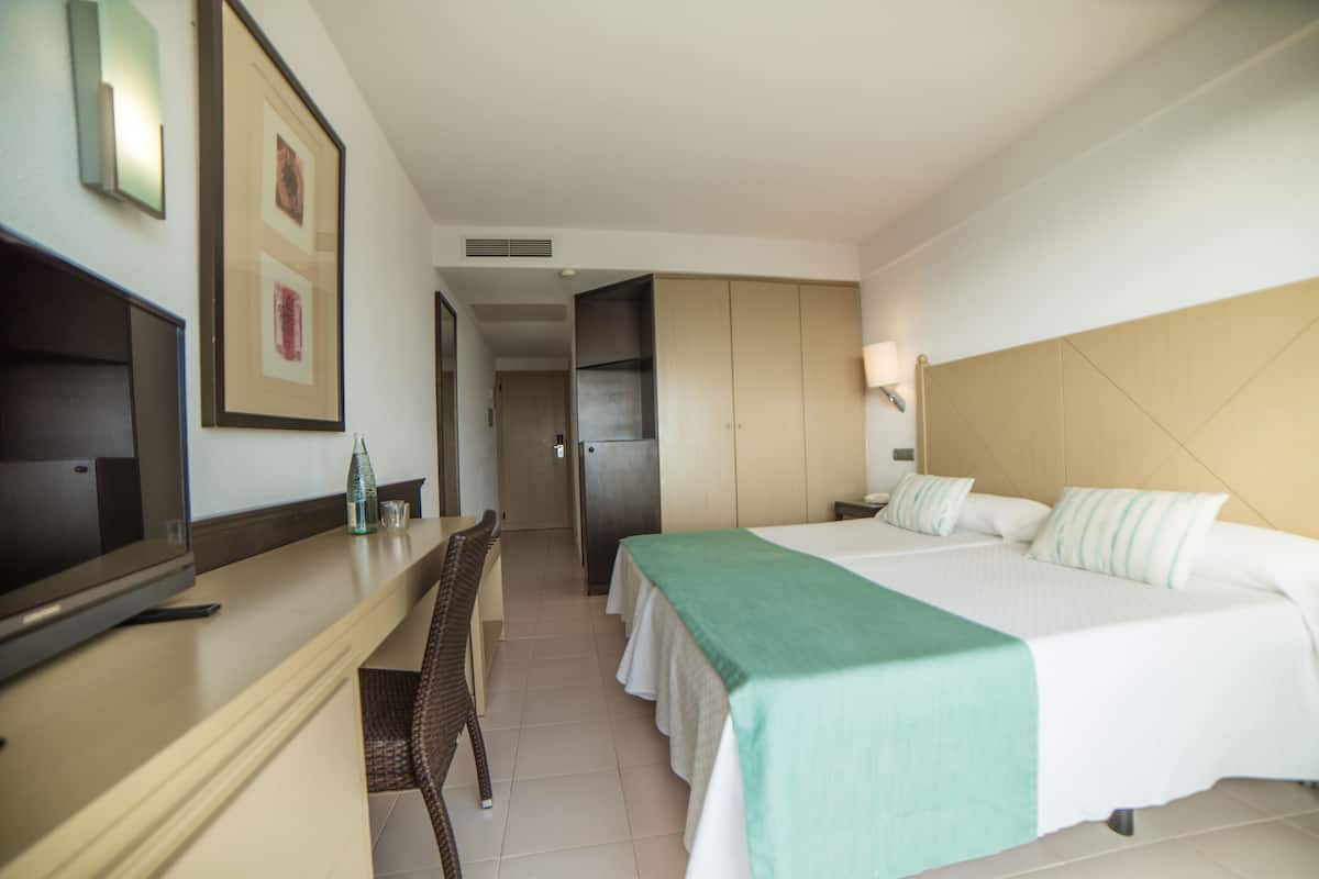 A hotel room with a bed, a desk with a TV, a chair, and a wardrobe.