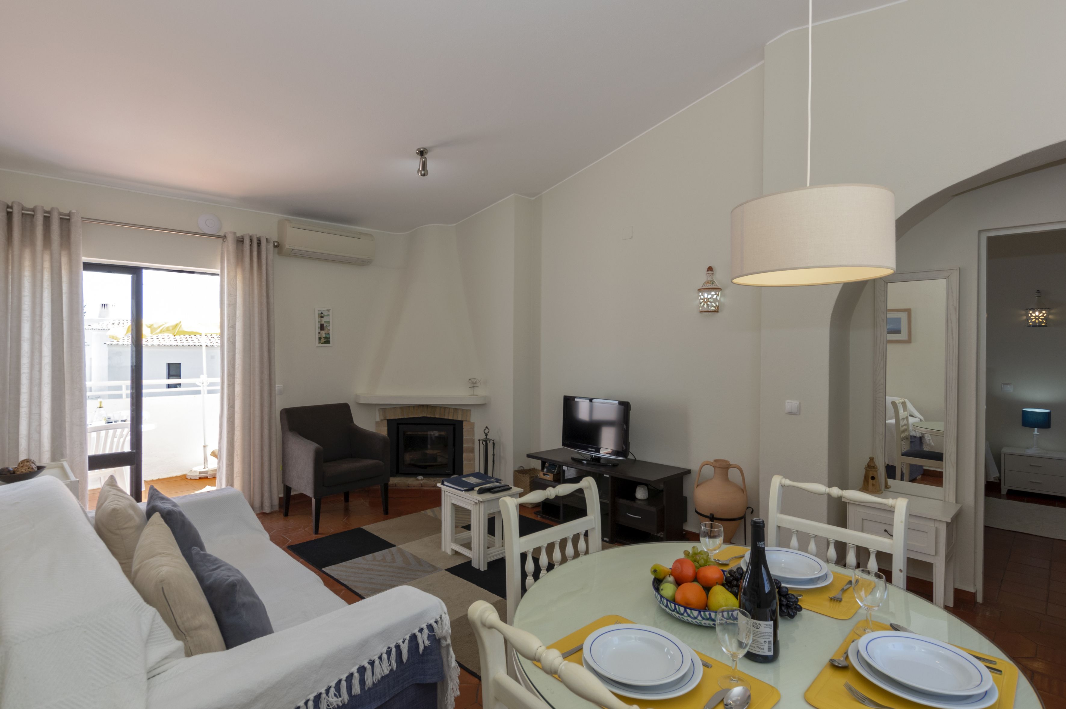 A modern living room with a sofa, a dining table set for four, a fireplace, and a television.