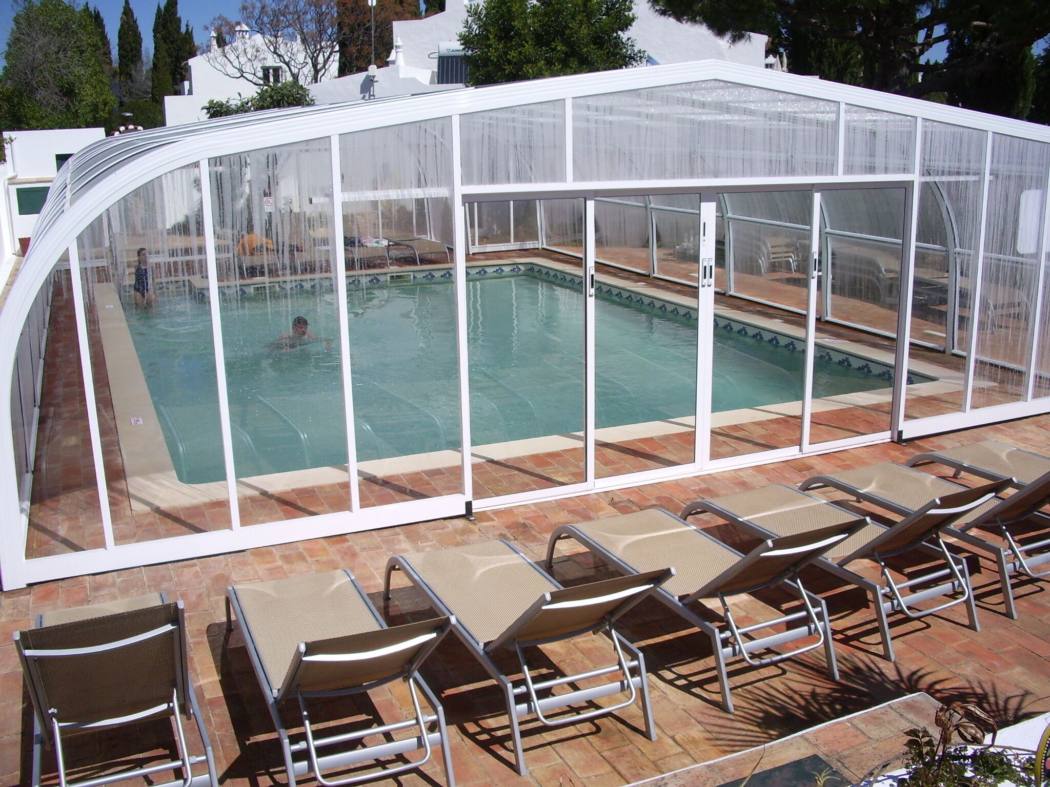 Una piscina con cerramiento de vidrio y sillas de descanso.
