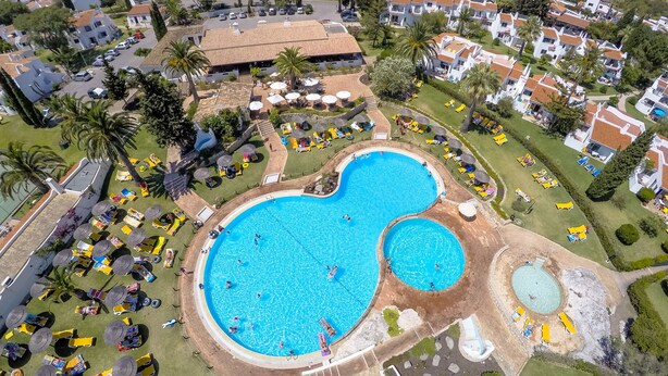 A large swimming pool surrounded by sun loungers and umbrellas, with a view of residential buildings in the background. - Rocha Brava Village Resort (Lagoa)