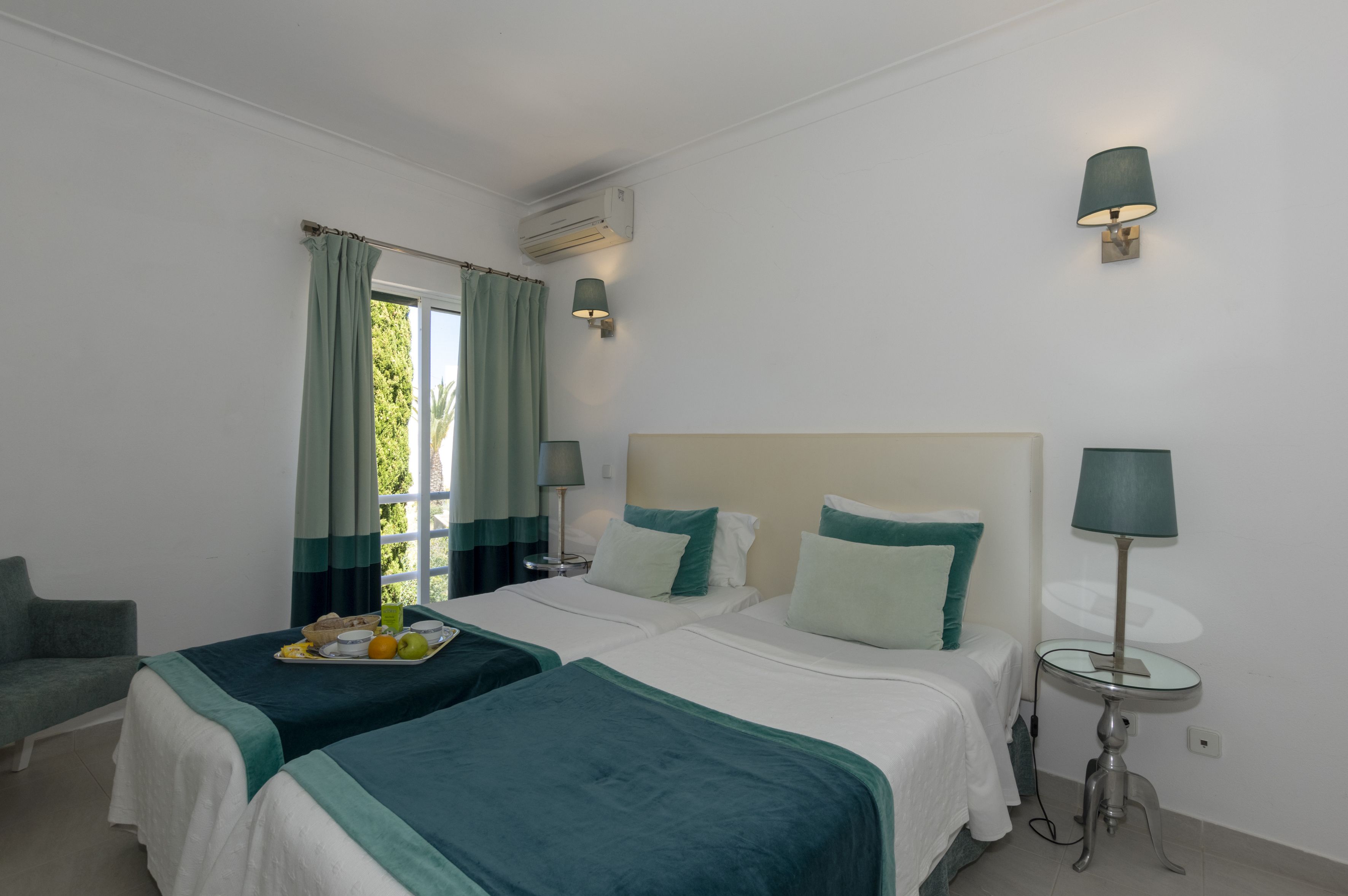 A hotel room with two beds, a chair, a table, and a lamp.