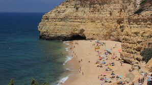 Una playa con aguas azules cristalinas, un acantilado rocoso y gente tomando el sol.