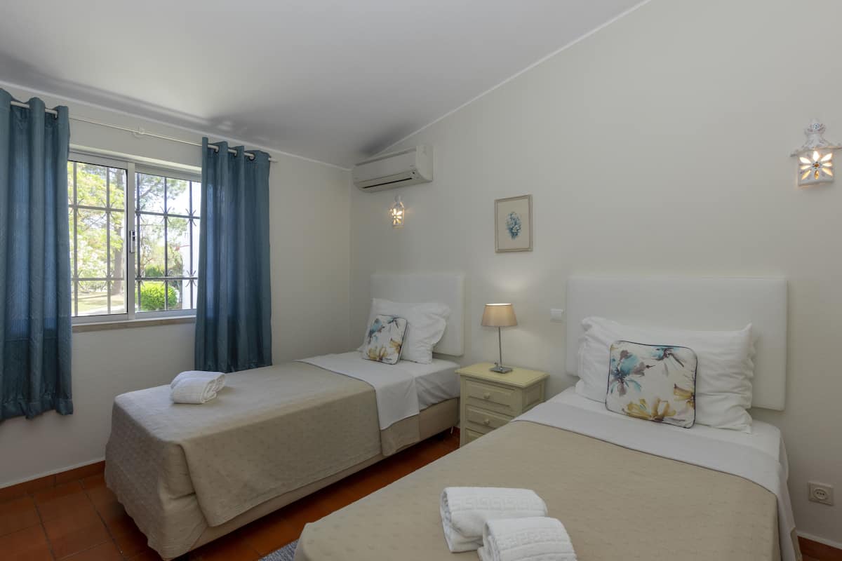 Une chambre d’hôtel avec deux lits, une fenêtre avec des rideaux, une table de chevet avec une lampe et un appareil de climatisation.