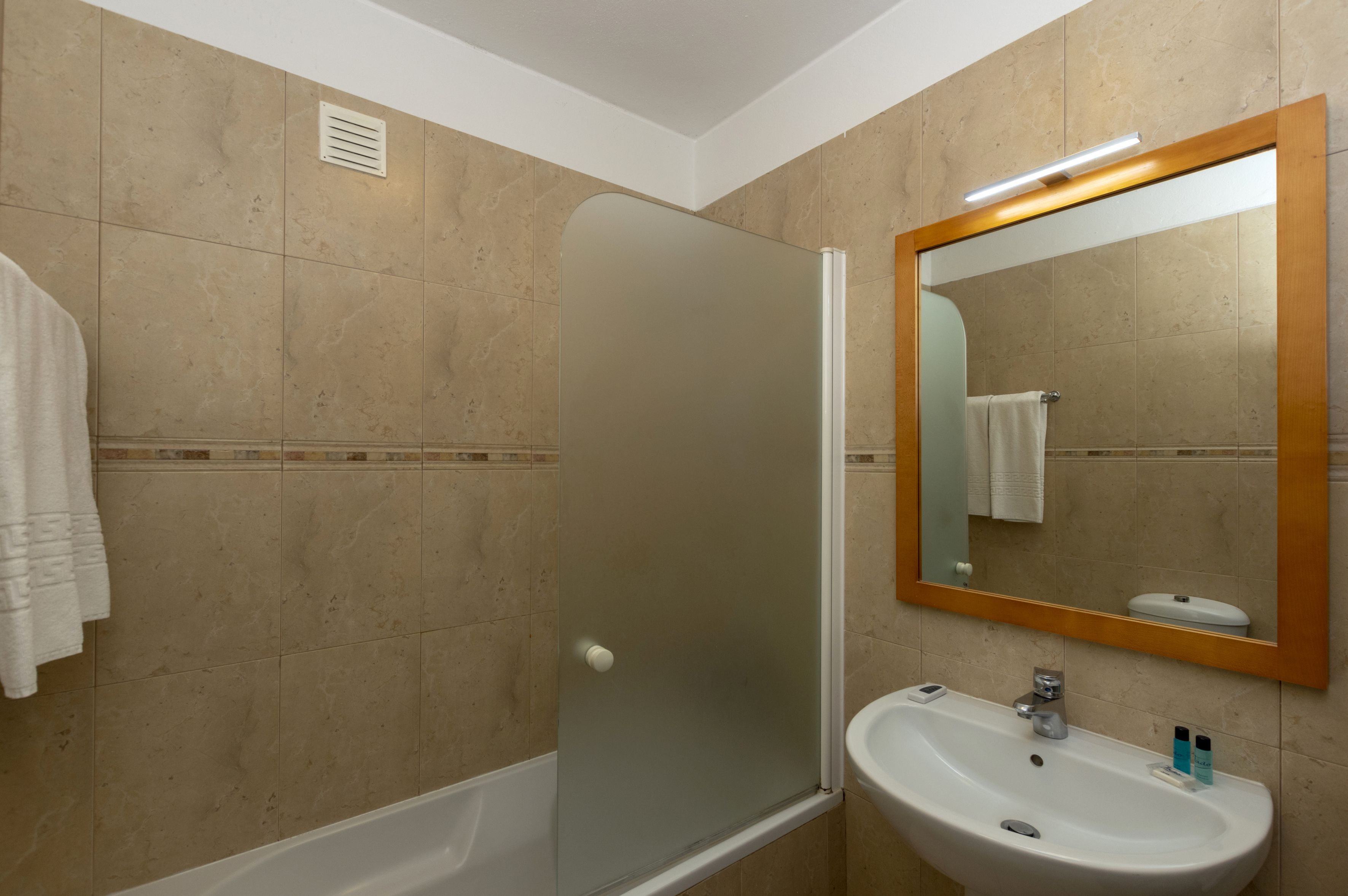 A bathroom with a glass-enclosed shower, a sink with a mirror, and beige tiled walls.