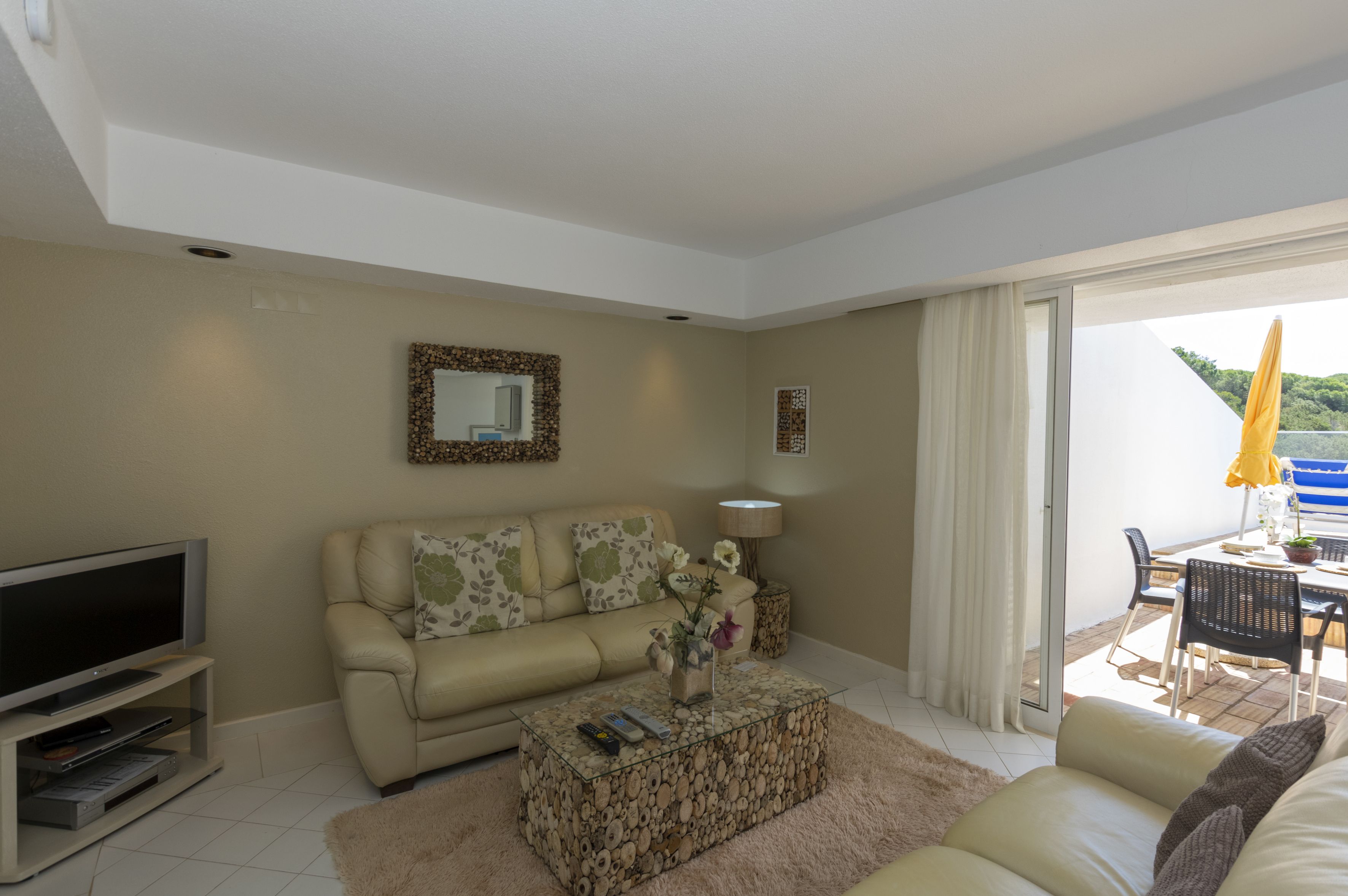 A modern living room with a sofa, a glass coffee table, a flat-screen TV, and a dining area with a table and chairs.