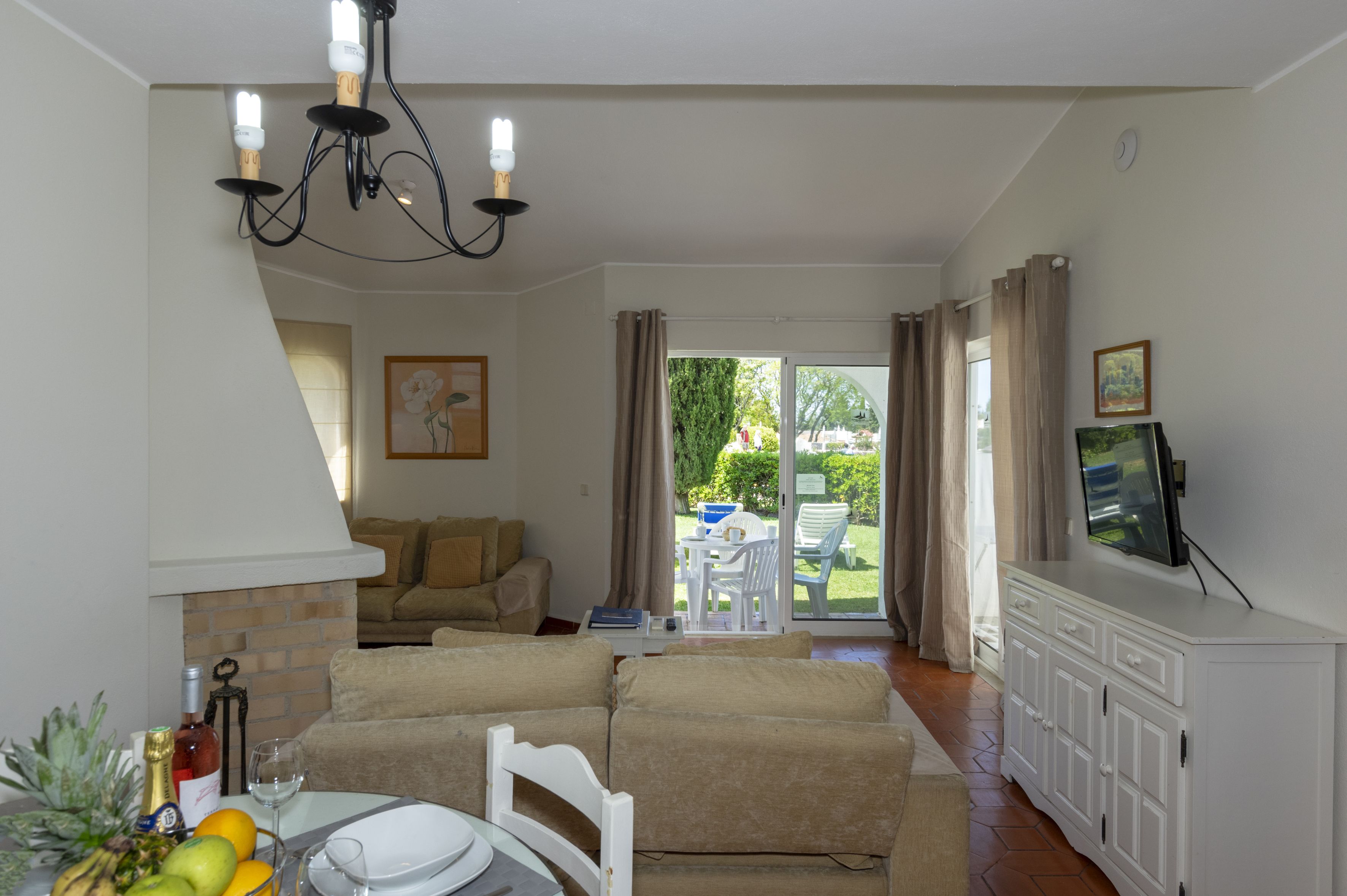 A living room with a sofa, a dining table with chairs, a TV on a cabinet, and a sliding glass door leading to a patio.