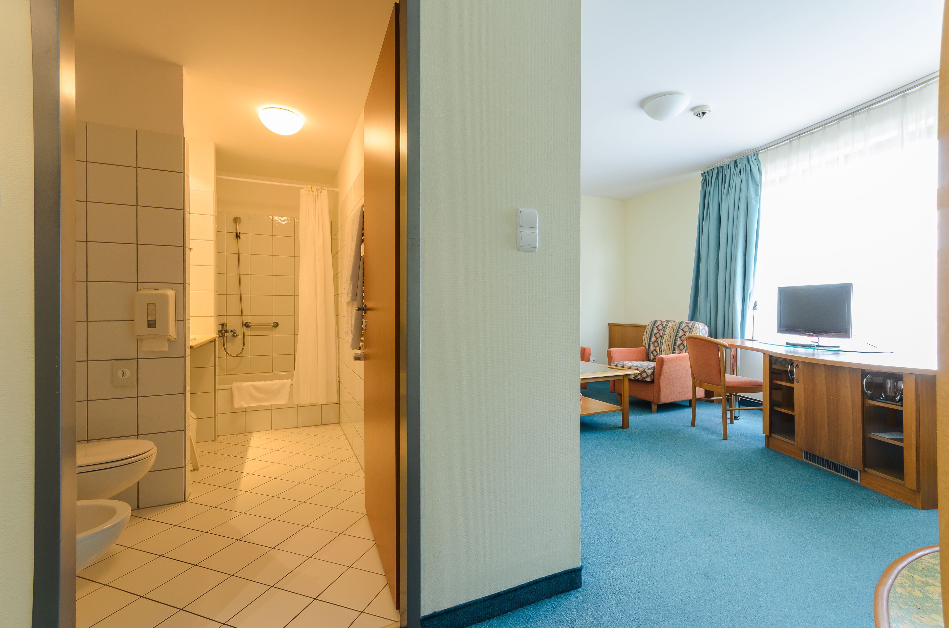 Quarto de hotel com banheiro, área de jantar e televisão.