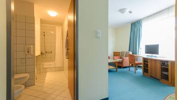 Quarto de hotel com banheiro, área de jantar e televisão.