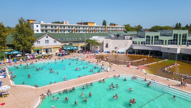 Un grand complexe de piscines extérieures comprenant plusieurs bassins et un bâtiment adjacent doté de balcons.