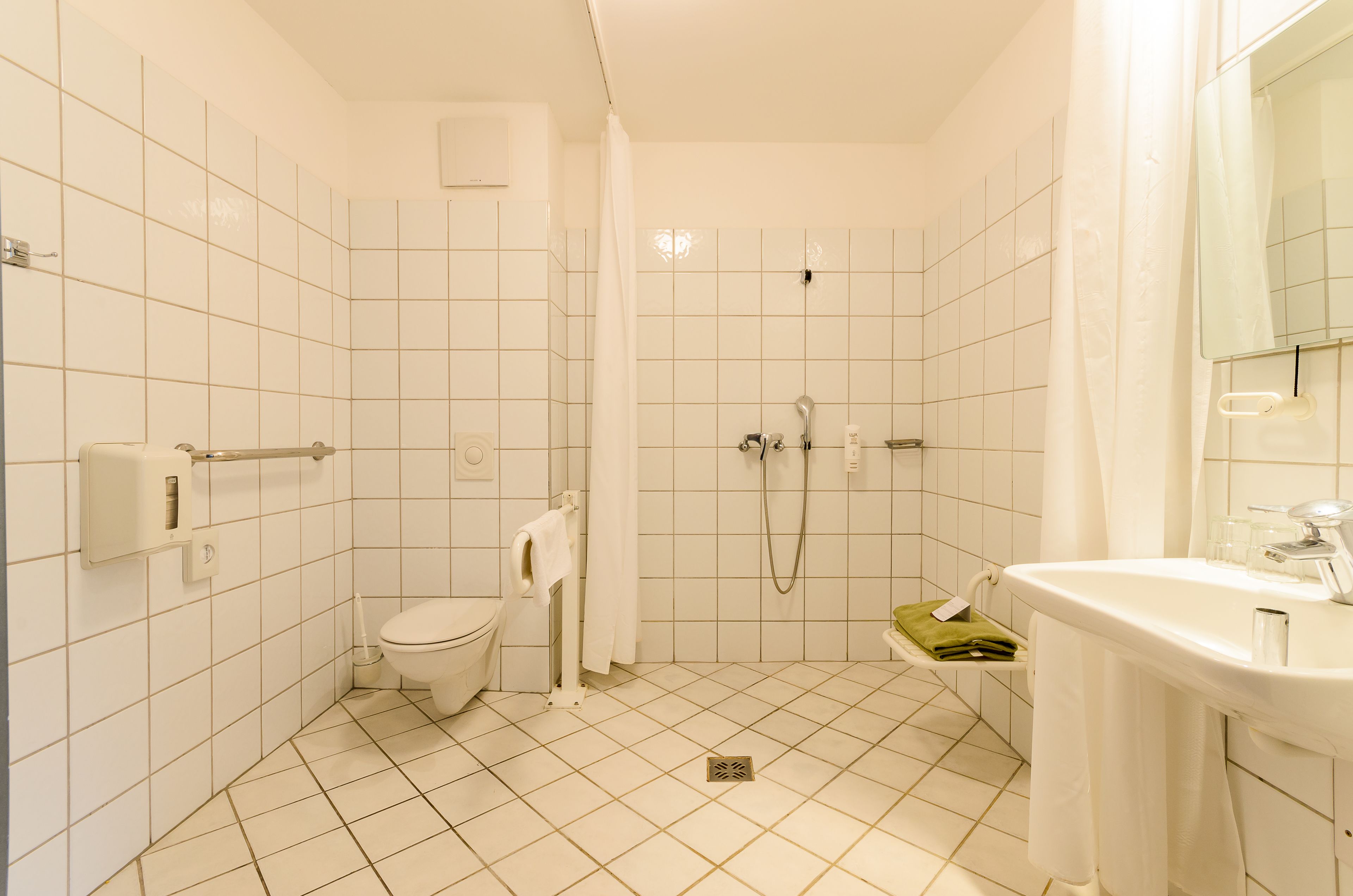 A bathroom with white tiled walls, a toilet, a shower with a glass door, and a sink with a mirror.