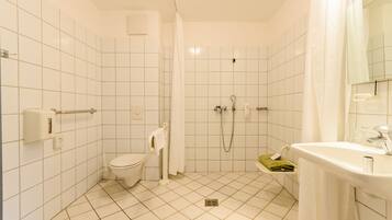 A bathroom with white tiled walls, a toilet, a shower with a glass door, and a sink with a mirror.