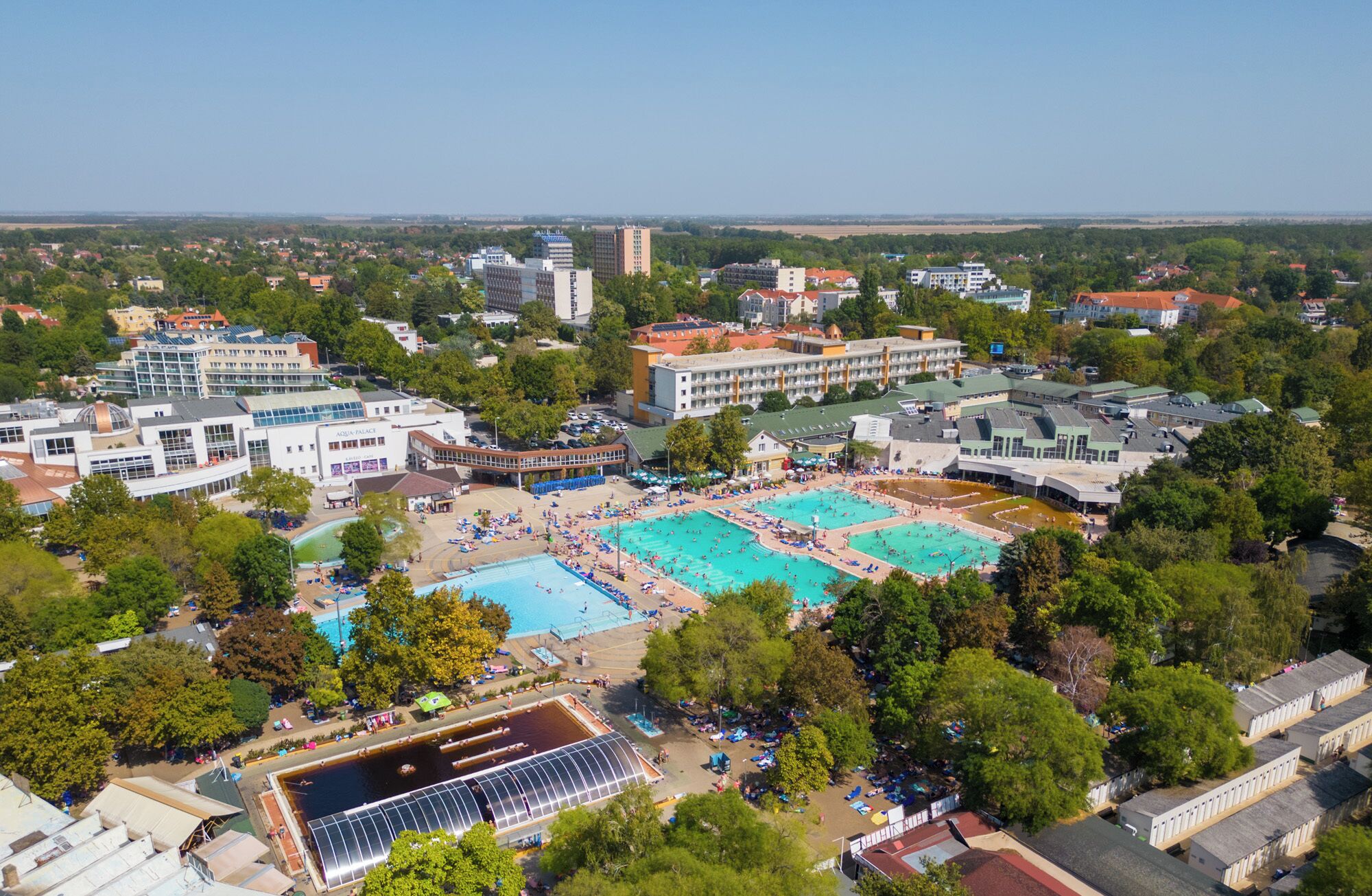 A large hotel complex with multiple swimming pools, a tennis court, and a greenhouse structure.