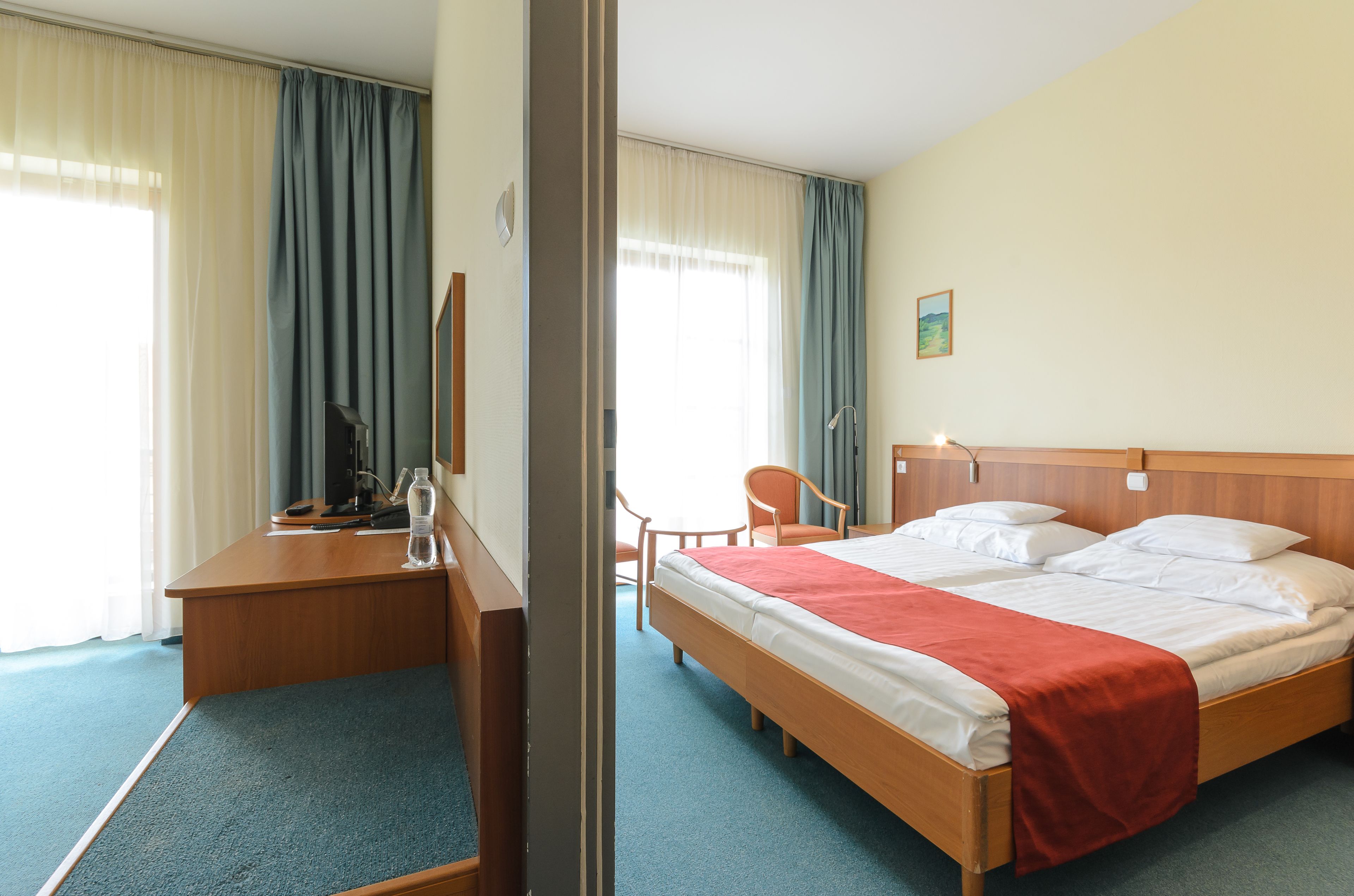 A hotel room with a bed, desk, chair, and a window with curtains.