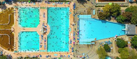 Vista aérea de un complejo de piscinas grande con varias piscinas y una zona circundante con sillas de playa y sombrillas.