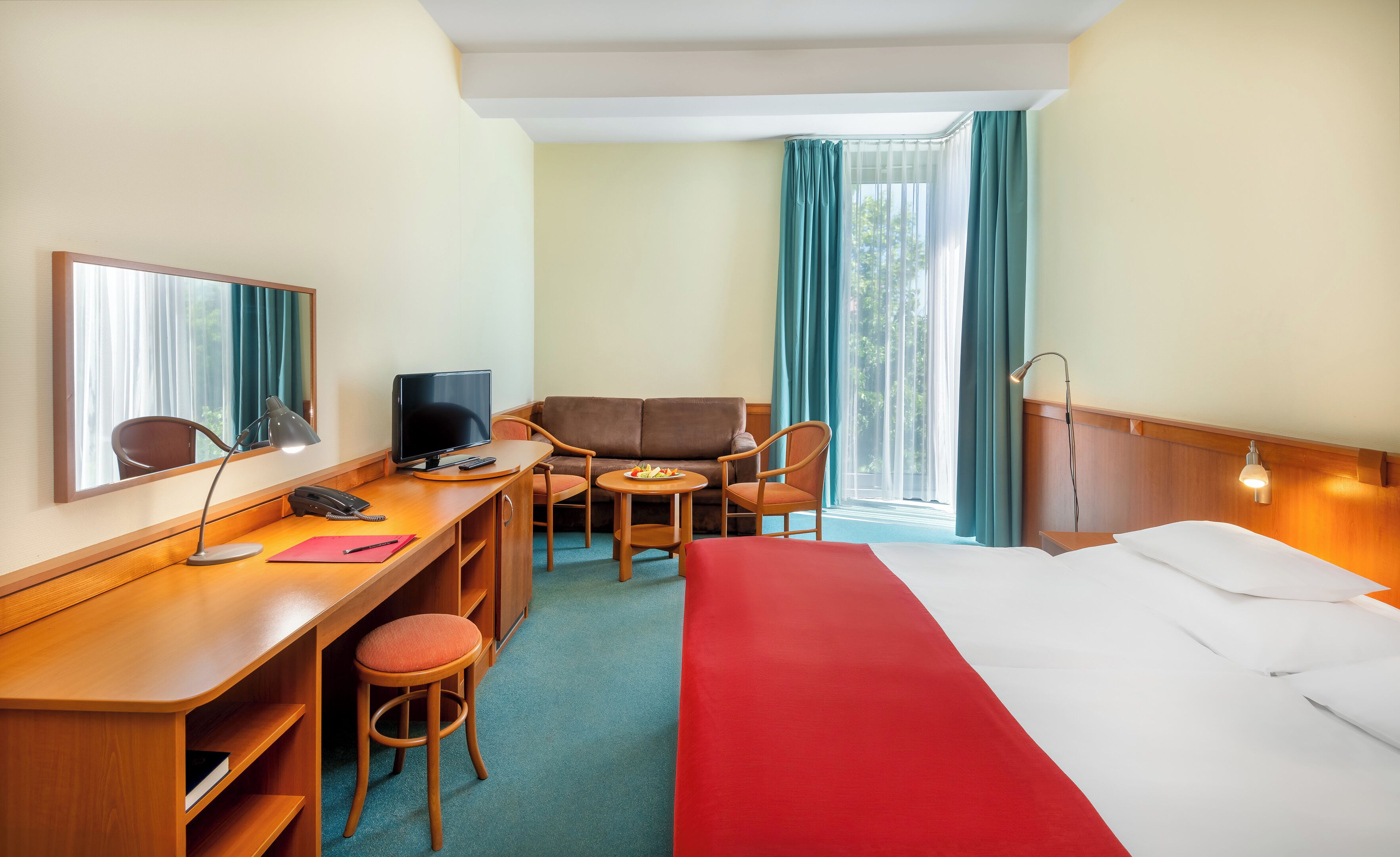 Quarto de hotel com cama, escrivaninha, cadeira e uma pequena mesa com um prato de fruta.