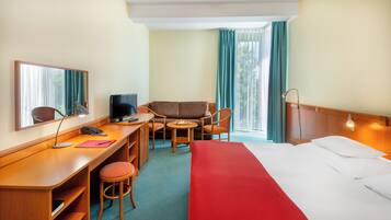 Quarto de hotel com cama, escrivaninha, cadeira e uma pequena mesa com um prato de fruta.