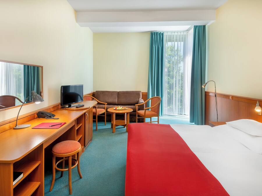 Quarto de hotel com cama, escrivaninha, cadeira e uma pequena mesa com um prato de fruta.
