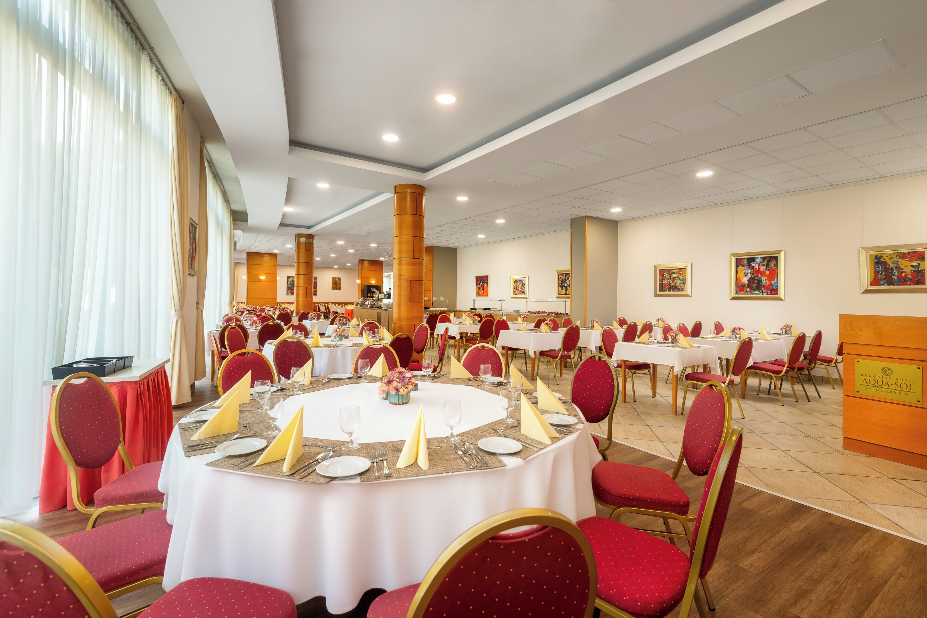 A banquet hall with round tables, red chairs, and white tablecloths.