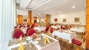 Un restaurant avec de nombreuses tables, des chaises rouges et des nappes blanches.