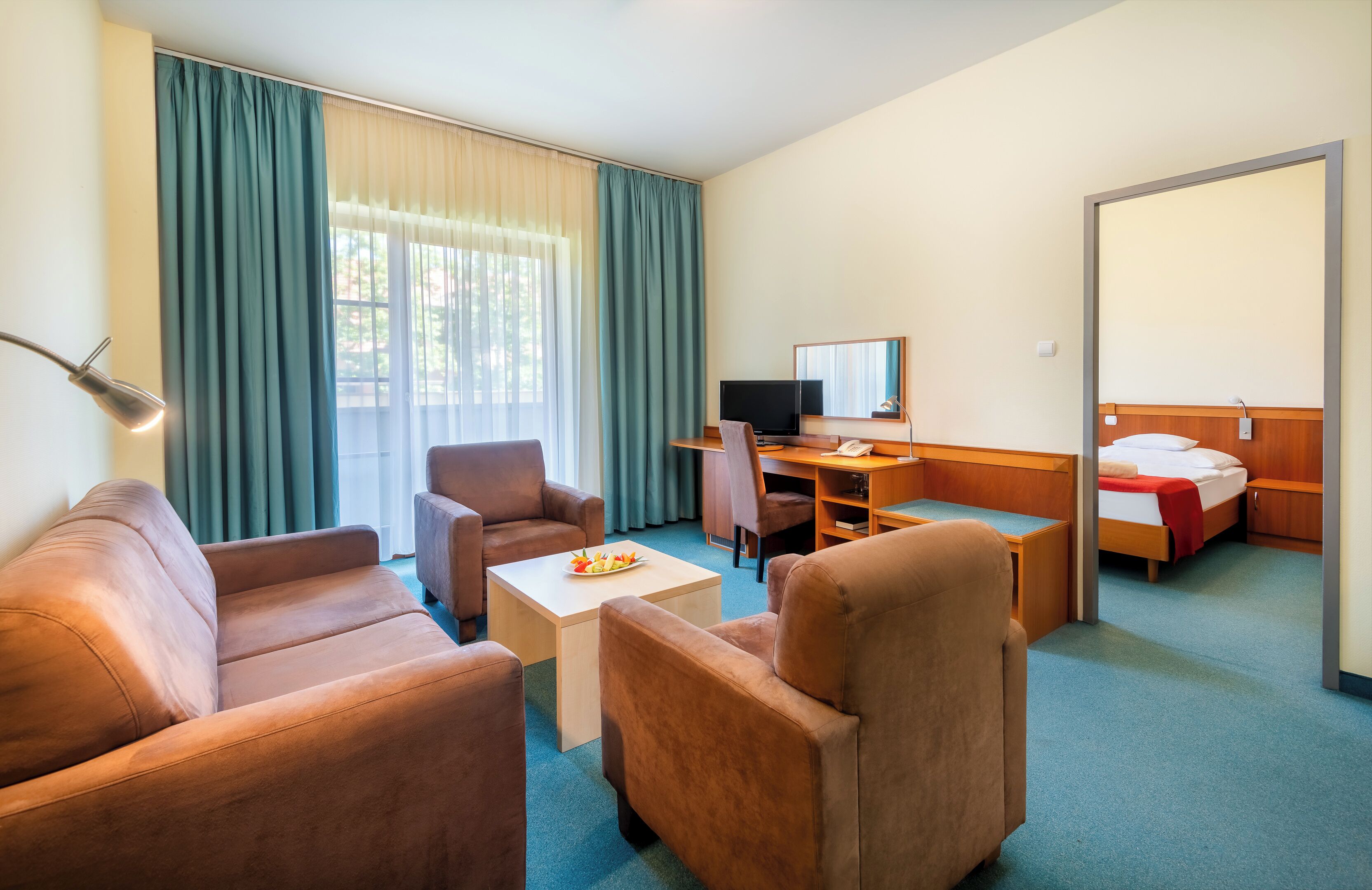 A hotel room with a sofa, armchairs, a desk with a computer, a bed, and a large mirror.