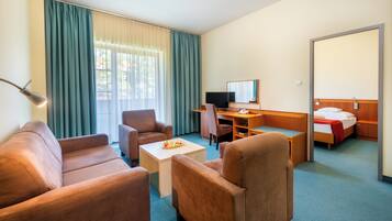 Habitación de hotel con sofá, sillones, un escritorio con computadora, cama y un espejo grande.