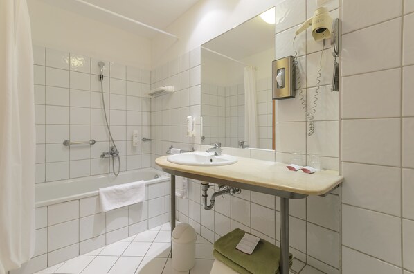 Un baño con bañera, lavamanos, espejo y un perchero para toallas.