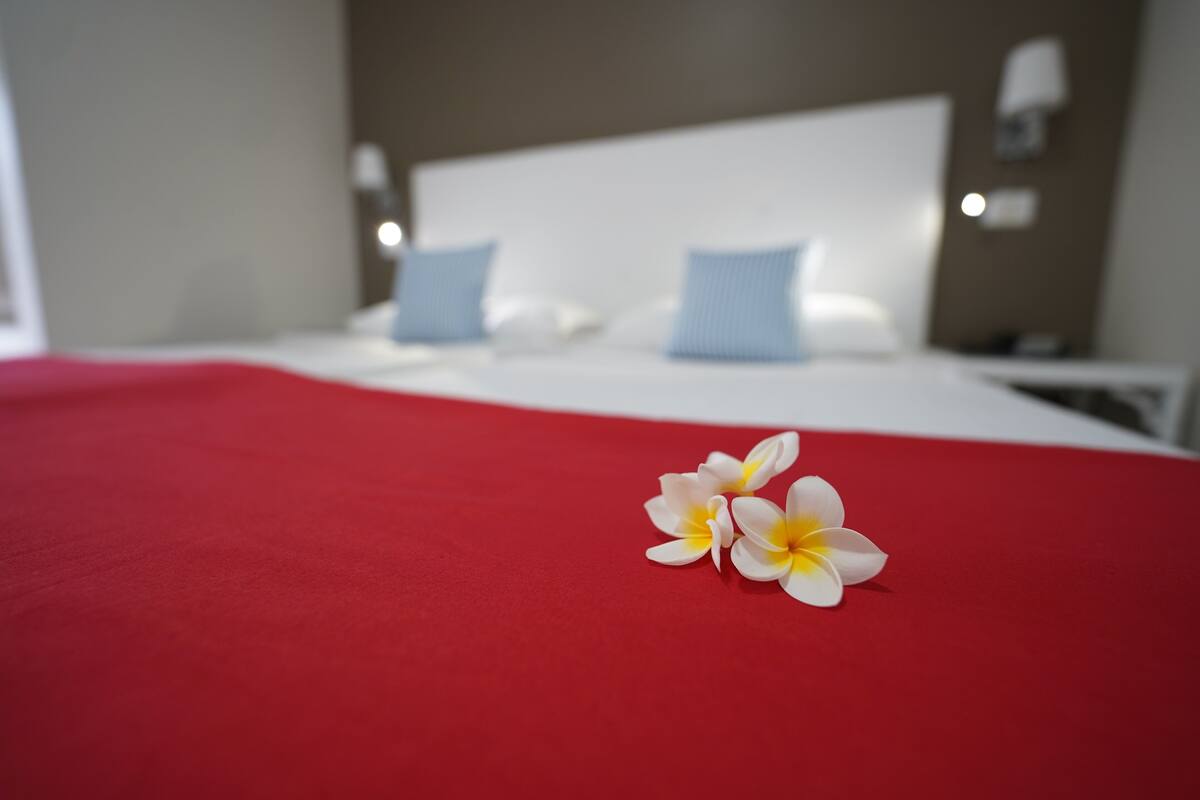 A bed with a red cover and two white and yellow flowers on it.