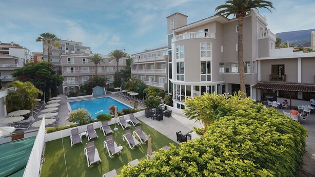 Un hôtel doté d’une piscine, de chaises longues et d’un jardin bien entretenu.