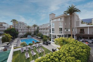 Een hotel met een zwembad, ligbedden en een verzorgde tuin.