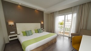 Une chambre d’hôtel avec un grand lit, un bureau, une chaise et un balcon avec des rideaux.