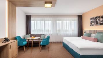 A hotel room with a bed, a desk, a chair, a small table, and a window with curtains.